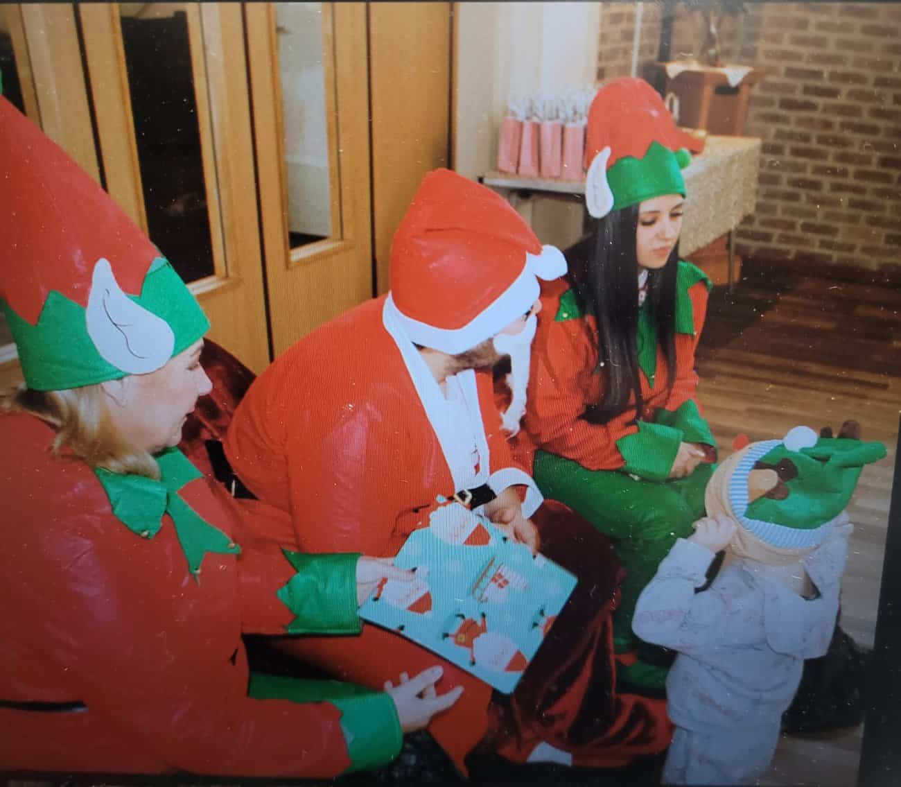 Santa and 2 elves siting giving a present to a small child