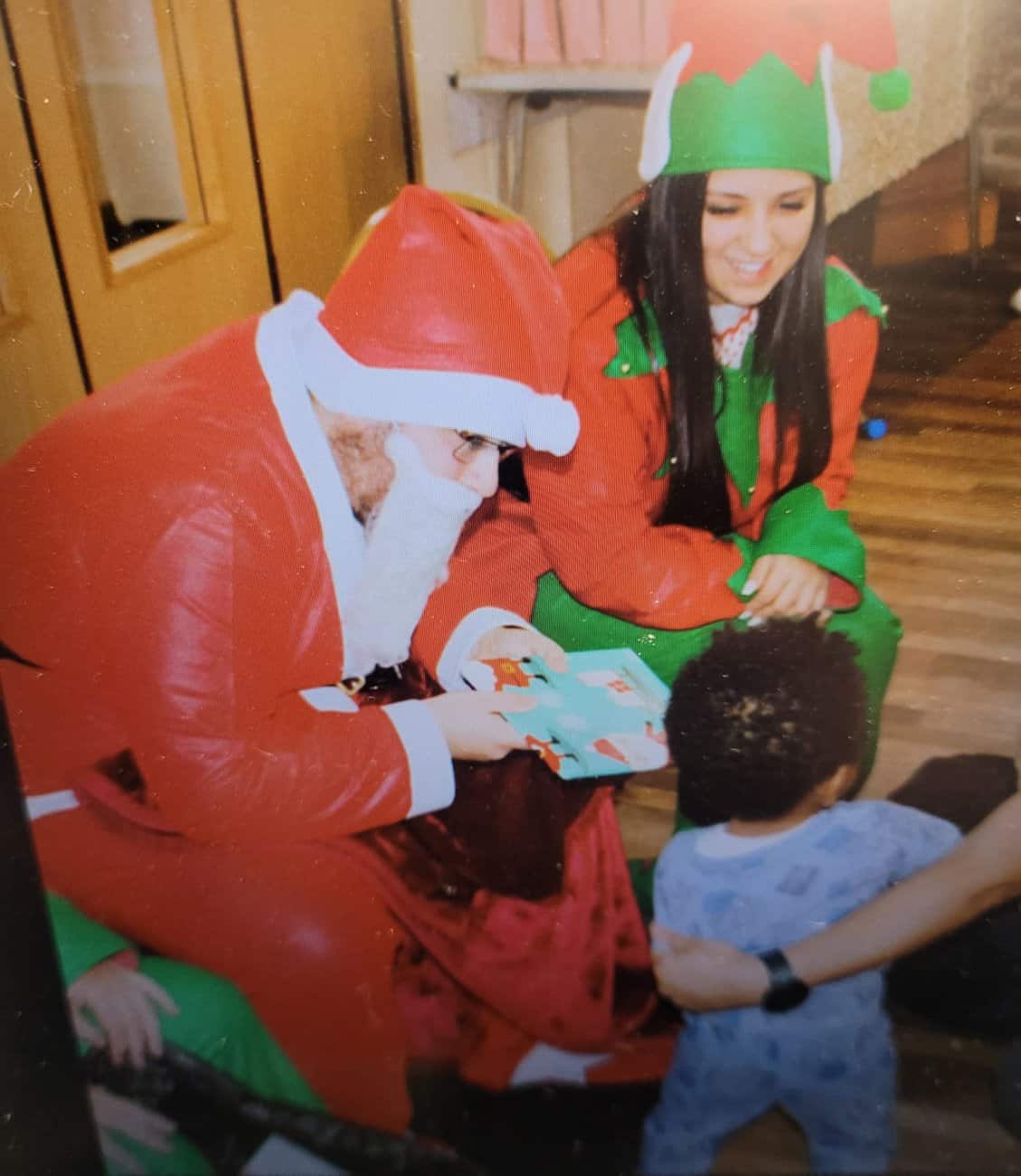 Santa and an elf siting giving a present to a small child
